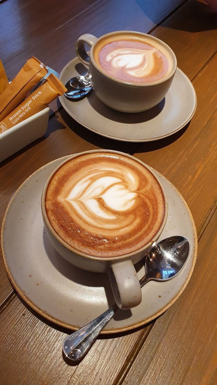 Dos capuchinos con arte latte servidos en mesa de madera